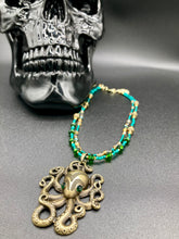 Load image into Gallery viewer, This Steampunk Brass Octopus Emerald Eyes Choker Style Necklace is an eye-catching piece for cosplay and gothic aficionados alike. Crafted with a large brass octopus pendant, emerald green eyes, and an adjustable glass beaded strand, this necklace is sure to turn heads. Featuring a range of light and dark green, gold, and brass tones, this necklace complements any sci-fi, fantasy, or steampunk ensemble. Measurements: 15 1/2” adjustable up to 17" in length