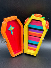 Load image into Gallery viewer, This coffin-shaped box features a bright royal blue exterior, with a bold sun and crescent adorning the center. Complemented with marigold flowers, the inside is painted in a bright red hue with turquoise and yellow cross detailing and traditional Mexican-themed fabric. Coffin Dimensions: Length: 4 1/2 Inches; Width: 2 1/2 inches; Height: 1 5/8 Inches