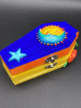 Load image into Gallery viewer, This coffin-shaped box features a bright royal blue exterior, with a bold sun and crescent adorning the center. Complemented with marigold flowers, the inside is painted in a bright red hue with turquoise and yellow cross detailing and traditional Mexican-themed fabric. Coffin Dimensions: Length: 4 1/2 Inches; Width: 2 1/2 inches; Height: 1 5/8 Inches