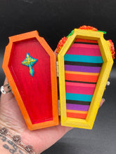 Load image into Gallery viewer, This coffin-shaped box features a bright royal blue exterior, with a bold sun and crescent adorning the center. Complemented with marigold flowers, the inside is painted in a bright red hue with turquoise and yellow cross detailing and traditional Mexican-themed fabric. Coffin Dimensions: Length: 4 1/2 Inches; Width: 2 1/2 inches; Height: 1 5/8 Inches