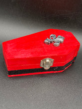 Load image into Gallery viewer, Super vibrant red coffin box has an eye-catching black and gray fleur de lis embellishment in the center, accompanied by a glittery black ribbon around the coffin. Inside, the interior is all black with a floral detailed black-silver cross.