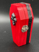 Load image into Gallery viewer, Super vibrant red coffin box has an eye-catching black and gray fleur de lis embellishment in the center, accompanied by a glittery black ribbon around the coffin. Inside, the interior is all black with a floral detailed black-silver cross.