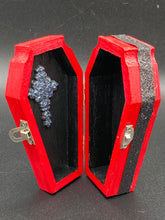Load image into Gallery viewer, Super vibrant red coffin box has an eye-catching black and gray fleur de lis embellishment in the center, accompanied by a glittery black ribbon around the coffin. Inside, the interior is all black with a floral detailed black-silver cross.
