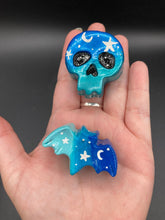Load image into Gallery viewer, Cute and spooky magnet design to adorn your refrigerator, lockers, workstation, toolbox, or dishwasher. This hand-sculpted clay skull and bat statuette boasts stunning ombre coloration, transitioning from dark blue to light blue to recreate the breathtaking look of a starry night sky.