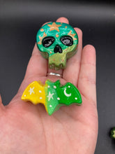 Load image into Gallery viewer, Cute and spooky magnet design to adorn your refrigerator, lockers, workstation, toolbox, or dishwasher. This hand-sculpted clay skull bat statuette boasts stunning ombre coloration, transitioning of dark green to light green to recreate the breathtaking look of a starry night sky. H 1” x W 2” x D 1/2”