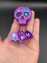 Load image into Gallery viewer, Cute and spooky magnet design to adorn your refrigerator, lockers, workstation, toolbox, or dishwasher. This hand-sculpted clay skull and  bat statuette boasts stunning ombre coloration, transitioning from dark purple to light purple to recreate the breathtaking look of a starry night sky. H 1” x W 2” x D 1/2”