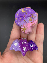 Load image into Gallery viewer, Cute and spooky magnet design to adorn your refrigerator, lockers, workstation, toolbox, or dishwasher. This hand-sculpted clay skull and bat statuette boasts stunning ombre coloration, transitioning from dark purple to light pink to recreate the breathtaking look of a starry night sky. H 1” x W 2” x D 1/2”