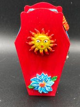 Load image into Gallery viewer, This coffin-shaped box features a bright red exterior, with a bold yellow, orange and red sun adorning the center. Complemented with a shimmery turquoise-blue ribbon and flower, the inside is painted in a dark royal blue hue with turquoise crescent moon detailing and traditional Mexican-themed fabric. Coffin Dimensions: Length: 4 1/2 Inches; Width: 2 1/2 inches; Height: 1 5/8 Inches