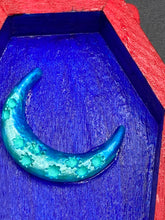 Load image into Gallery viewer, This coffin-shaped box features a bright red exterior, with a bold yellow, orange and red sun adorning the center. Complemented with a shimmery turquoise-blue ribbon and flower, the inside is painted in a dark royal blue hue with turquoise crescent moon detailing and traditional Mexican-themed fabric. Coffin Dimensions: Length: 4 1/2 Inches; Width: 2 1/2 inches; Height: 1 5/8 Inches