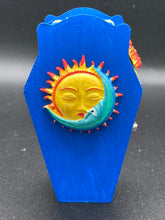Load image into Gallery viewer, This coffin-shaped box features a bright royal blue exterior, with a bold sun and crescent adorning the center. Complemented with a shimmery pastel-yellow ribbon and flower, the inside is painted in a canary yellow hue with turquoise crescent moon detailing and traditional Mexican-themed fabric. Coffin Dimensions: Length: 4 1/2 Inches; Width: 2 1/2 inches; Height: 1 5/8 Inches
