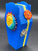 Load image into Gallery viewer, This coffin-shaped box features a bright royal blue exterior, with a bold sun and crescent adorning the center. Complemented with a shimmery pastel-yellow ribbon and flower, the inside is painted in a canary yellow hue with turquoise crescent moon detailing and traditional Mexican-themed fabric. Coffin Dimensions: Length: 4 1/2 Inches; Width: 2 1/2 inches; Height: 1 5/8 Inches