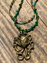 Load image into Gallery viewer, This Steampunk Brass Octopus Emerald Eyes Choker Style Necklace is an eye-catching piece for cosplay and gothic aficionados alike. Crafted with a large brass octopus pendant, emerald green eyes, and an adjustable glass beaded strand, this necklace is sure to turn heads. Featuring a range of light and dark green, gold, and brass tones, this necklace complements any sci-fi, fantasy, or steampunk ensemble. Measurements: 15 1/2” adjustable up to 17" in length