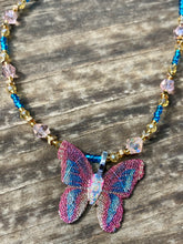 Load image into Gallery viewer, This delicate butterfly pendant is crafted from a basil leaf and adorned with accents of pink, gold and blue. A shining glass beaded necklace crafted from beads of varying shades of pink, gold, and blue, creates a beautiful accompaniment to the butterfly wings. Wear this ravishing necklace and butterfly jewelry pendant to embody the spirit of warm Spring and Summer days. 16 1/4” in length adjustable up to 18"