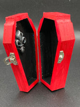 Load image into Gallery viewer, This unique ring box is sure to make an impression, with its simple but vibrant red coffin design and eye-catching black and gray floral cross in the center. The interior is black with a detailed fleur de lis, making the perfect resting place for your voodoo doll. It's spooky but also cute, with its accompanying Misfit VooDoo Doll.