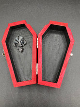 Load image into Gallery viewer, This unique ring box is sure to make an impression, with its simple but vibrant red coffin design and eye-catching black and gray floral cross in the center. The interior is black with a detailed fleur de lis, making the perfect resting place for your voodoo doll. It's spooky but also cute, with its accompanying Misfit VooDoo Doll.