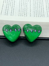 Load image into Gallery viewer, Perfect cute and spooky Halloween item to add to your fridge, locker, cubicle or toolbox. This hand-crafted light and dark green heart-shaped magnet showcases a Frankenstein-inspired design. Measurements: H 1 1/2” x W 1 5/8” x D 1/2”