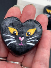 Load image into Gallery viewer, Perfect cute and spooky Halloween magnet art to add to your fridge, locker, cubicle or toolbox. This hand-crafted heart-shaped magnet features a figurine of a black cat with distinctive yellow eyes. Measurements: H 1 1/2” x W 1 5/8” x D 1/2”
