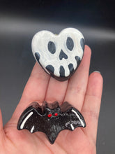 Load image into Gallery viewer, Perfect cute and spooky Halloween magnet art to add to your fridge, locker, cubicle or toolbox.  This hand-crafted black heart-shaped magnet features a white skull figurine  with distinctive black eyes. Cute all black bat with white highlights with red eyes magnet.