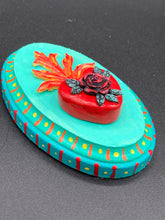 Load image into Gallery viewer, This Sacred Heart Wall Art Decor is the perfect way to enhance your home with an artistic flair. This beautiful artwork features a bright turquoise wooden frame with a hand-crafted bright red heart. The heart is detailed with dark red rose and vibrant green leaves, with a vibrant fire embellishment over the center. Gold decorative embellishments at the sides of the heart add a luxurious touch. H 5 3/8" x W 3 3/8” x D 1 1/2"