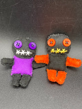 Load image into Gallery viewer, Short and tiny black and purple Voodoo Doll is 3" in height. Torso is purple while legs and arms and head are all black like the night. He has matching purple buttons for eyes and has a sowed shut mouth. Short and tiny black and orange Voodoo Doll is 3" in height. Torso and head is all black while legs and arms are bright orange, perfect Halloween colors. He has matching bright orange buttons for eyes and has a sowed shut mouth.