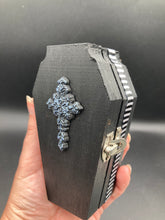 Load image into Gallery viewer, This unique vintage-inspired ring box is perfect for storing your jewelry and other special items. The wood coffin design is accented with a detailed floral black silver cross and a white and black ribbon. The interior is lined with a skull fabric and a fleur de lis embellishment, adding a spooky yet cute flair.