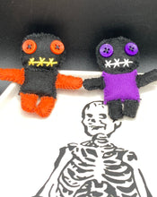 Load image into Gallery viewer, Short and tiny black and purple Voodoo Doll is 3" in height. Torso is purple while legs and arms and head are all black like the night. He has matching purple buttons for eyes and has a sowed shut mouth. Short and tiny black and orange Voodoo Doll is 3" in height. Torso and head is all black while legs and arms are bright orange, perfect Halloween colors. He has matching bright orange buttons for eyes and has a sowed shut mouth.