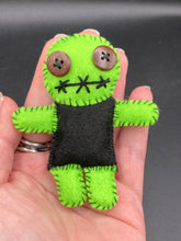 Load image into Gallery viewer, Black And Green Voodoo Doll stand at 3 3/8" in height. Torso is black, while his arms, legs and head is all lime green. He has stylish brown buttons for eyes. Adorable but with a dash of creepy.