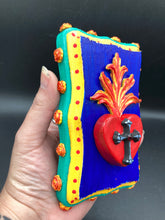 Load image into Gallery viewer, This Sacred Heart Wall Art Decor is the perfect way to enhance your home with an artistic flair. This Sacred Heart Wall Art Decor is crafted with a stunning red heart detailed with a black-silver cross and a vibrant fire embellishment at its center. Adding to its unique traditional Mexican aesthetic, the wood frame is decorated with marigold flowers, creating a beautiful and eye-catching artwork.