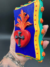 Load image into Gallery viewer, This Sacred Heart Wall Art Decor is the perfect way to enhance your home with an artistic flair. This Sacred Heart Wall Art Decor is crafted with a stunning red heart detailed with a black-silver cross and a vibrant fire embellishment at its center. Adding to its unique traditional Mexican aesthetic, the wood frame is decorated with marigold flowers, creating a beautiful and eye-catching artwork.