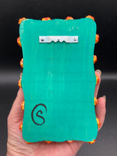 Load image into Gallery viewer, This Sacred Heart Wall Art Decor is the perfect way to enhance your home with an artistic flair. This Sacred Heart Wall Art Decor is crafted with a stunning red heart detailed with a black-silver cross and a vibrant fire embellishment at its center. Adding to its unique traditional Mexican aesthetic, the wood frame is decorated with marigold flowers, creating a beautiful and eye-catching artwork.