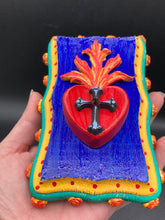 Load image into Gallery viewer, This Sacred Heart Wall Art Decor is the perfect way to enhance your home with an artistic flair. This Sacred Heart Wall Art Decor is crafted with a stunning red heart detailed with a black-silver cross and a vibrant fire embellishment at its center. Adding to its unique traditional Mexican aesthetic, the wood frame is decorated with marigold flowers, creating a beautiful and eye-catching artwork.