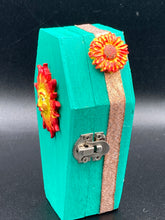Load image into Gallery viewer, This coffin-shaped box features a bright turquoise exterior, with a bold yellow, orange and red sun adorning the center. Complemented with a shimmery rose-gold ribbon and flower, the inside is painted in a vibrant orange hue with turquoise crescent moon detailing and traditional Mexican-themed fabric. Coffin Dimensions: Length: 4 1/2 Inches; Width: 2 1/2 inches; Height: 1 5/8 Inches