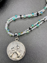 Load image into Gallery viewer, This stylish necklace features a shimmery sterling silver quartz pendant with cats and stars, making it the perfect accessory for any cat lover. With two-hole silver and black beads that stand out against the light aquamarine glass beads, this double strand necklace holds a round kitty pendant made with various hues of clear and iridescent glass beads. Add a touch of purrfection to your look with this statement piece. Measurements: Necklace is 15”adjustable up to 18"