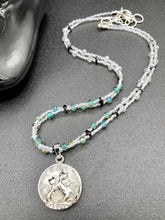Load image into Gallery viewer, This stylish necklace features a shimmery sterling silver quartz pendant with cats and stars, making it the perfect accessory for any cat lover. With two-hole silver and black beads that stand out against the light aquamarine glass beads, this double strand necklace holds a round kitty pendant made with various hues of clear and iridescent glass beads. Add a touch of purrfection to your look with this statement piece. Measurements: Necklace is 15”adjustable up to 18"