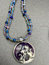 Load image into Gallery viewer, This stylish necklace features a shimmery sterling silver amethys pendant with cats and stars, making it the perfect accessory for any cat lover. With two-hole blue beads compliments the dark dark purple hues glass beads, this double strand necklace holds a round kitty pendant made with various hues of purple, blue and gold tone glass beads. Add a touch of purrfection to your look with this statement piece.   Measurements:  Necklace is 15 1/2” adjustable up to 18"