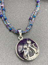 Load image into Gallery viewer, This stylish necklace features a shimmery sterling silver amethys pendant with cats and stars, making it the perfect accessory for any cat lover. With two-hole blue beads compliments the dark dark purple hues glass beads, this double strand necklace holds a round kitty pendant made with various hues of purple, blue and gold tone glass beads. Add a touch of purrfection to your look with this statement piece.   Measurements:  Necklace is 15 1/2” adjustable up to 18"