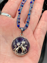 Load image into Gallery viewer, This stylish necklace features a shimmery sterling silver amethys pendant with cats and stars, making it the perfect accessory for any cat lover. With two-hole blue beads compliments the dark dark purple hues glass beads, this double strand necklace holds a round kitty pendant made with various hues of purple, blue and gold tone glass beads. Add a touch of purrfection to your look with this statement piece.   Measurements:  Necklace is 15 1/2” adjustable up to 18"