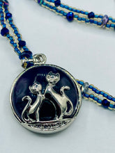Load image into Gallery viewer, This stylish necklace features a shimmery sterling silver amethys pendant with cats and stars, making it the perfect accessory for any cat lover. With two-hole blue beads compliments the dark dark purple hues glass beads, this double strand necklace holds a round kitty pendant made with various hues of purple, blue and gold tone glass beads. Add a touch of purrfection to your look with this statement piece.   Measurements:  Necklace is 15 1/2” adjustable up to 18"
