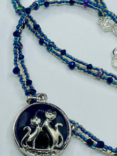 Load image into Gallery viewer, This stylish necklace features a shimmery sterling silver amethys pendant with cats and stars, making it the perfect accessory for any cat lover. With two-hole blue beads compliments the dark dark purple hues glass beads, this double strand necklace holds a round kitty pendant made with various hues of purple, blue and gold tone glass beads. Add a touch of purrfection to your look with this statement piece.   Measurements:  Necklace is 15 1/2” adjustable up to 18"