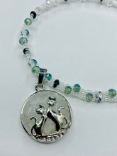 Load image into Gallery viewer, This stylish necklace features a shimmery sterling silver quartz pendant with cats and stars, making it the perfect accessory for any cat lover. With two-hole silver and black beads that stand out against the light aquamarine glass beads, this double strand necklace holds a round kitty pendant made with various hues of clear and iridescent glass beads. Add a touch of purrfection to your look with this statement piece. Measurements: Necklace is 15”adjustable up to 18"