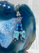 Load image into Gallery viewer, Glass beaded earrings take center stage in this design, with light blue glass beads as the primary color. These beads contain varying shades of blue, purple, and a hint of gold to add interest and texture to the style. As a show-stopping accessory, this piece of jewelry is a must-have for any collection. Measurements: 1 3/8” in length