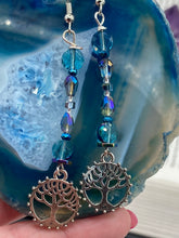 Load image into Gallery viewer, This captivating set of earrings boasts an exquisite range of intense blues and purples, accented with a warm touch of gold and green. The dangling silver plated tree of life charm adds a beautiful finishing touch. Measurements: 2 1/2” in length