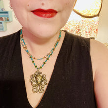 Load image into Gallery viewer, This Steampunk Brass Octopus Emerald Eyes Choker Style Necklace is an eye-catching piece for cosplay and gothic aficionados alike. Crafted with a large brass octopus pendant, emerald green eyes, and an adjustable glass beaded strand, this necklace is sure to turn heads. Featuring a range of light and dark green, gold, and brass tones, this necklace complements any sci-fi, fantasy, or steampunk ensemble. Measurements: 15 1/2” adjustable up to 17" in length