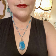 Load image into Gallery viewer, This Vibrant Sea Blue Agate Natural Stone Pendant Choker Style Beaded Necklace includes two strands of glass beads in shades of blues, silver and clear to lend shimmer and color to this large stone pendant. The shorter strand consists of very light blue small glass beads, while the longer strand is primarily a light baby blue. A set of dainty matching earrings completes the look. This beautiful gemstone necklace is the perfect accessory to bring the beach with you in the coming months.