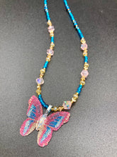 Load image into Gallery viewer, This delicate butterfly pendant is crafted from a basil leaf and adorned with accents of pink, gold and blue. A shining glass beaded necklace crafted from beads of varying shades of pink, gold, and blue, creates a beautiful accompaniment to the butterfly wings. Wear this ravishing necklace and butterfly jewelry pendant to embody the spirit of warm Spring and Summer days. 16 1/4” in length adjustable up to 18"