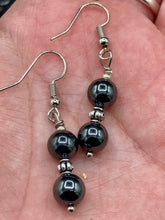 Load image into Gallery viewer, Elevate your boho chic style with these beautiful hematite and glass beaded earrings. Featuring two hematite round beads and a floral silver metal bead in the middle, these earrings offer a stylish and chic touch to any outfit.  Measurements: 1 1/4” in length