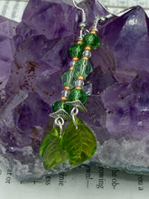 Load image into Gallery viewer, Long strand of glittering light green and gold glass beads, as well as a leaf-shaped glass charm at the bottom, combine to create a highly dynamic effect. These versatile earrings, perfect for a whimsical fairy princess, good witch, or nature-loving hippie look, draw on nature-inspired designs, providing the ideal finishing touch to any ensemble. Measurements: 2 1/4” in length