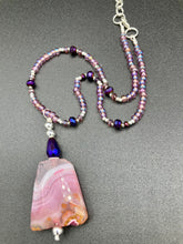 Load image into Gallery viewer, A soft dusty rose agate pendant is accompanied by shimmery beads of dusty rose, blue, dark pink, and gold. Adorned with large deep purple glass beads with a hint of gold shimmer, this stunning necklace set evokes a rose garden. Measurements: Necklace is 15” adjustable to 18"