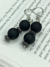 Load image into Gallery viewer, These flat matte black round glass bead earrings with silver plated floral beads offer a versatile look perfect for cocktail chic attire, a wedding necklace, and minimalist style. Measurements: 1 1/4” in length