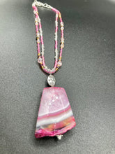 Load image into Gallery viewer, This large agate pendant features a variety of pink hues, from light to dark, and is accompanied by two strands of glass beaded necklaces with pink, silver, gold, and clear beads. The combination of colors creates a stunning and vibrant look, perfect for accessorizing any summer look. Measurements: Necklace is 15” adjustable up to 18" in length